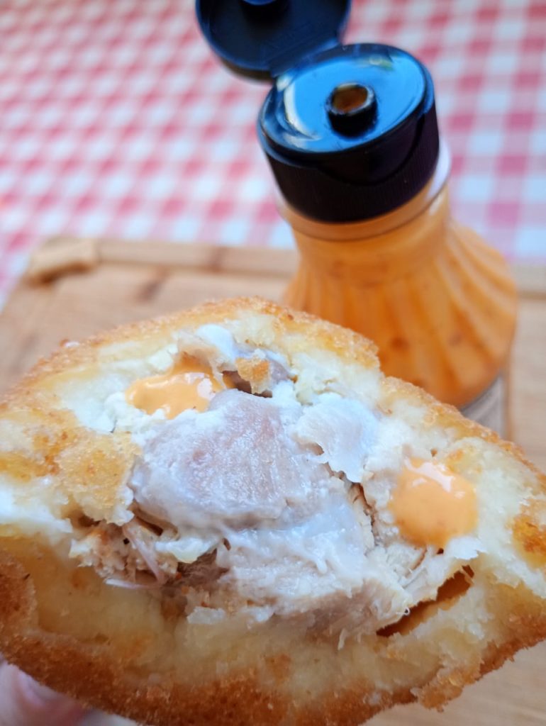 Coxa creme com mordida, revelando o recheio cremoso, servida ao lado de um pequeno vidro de pimenta.